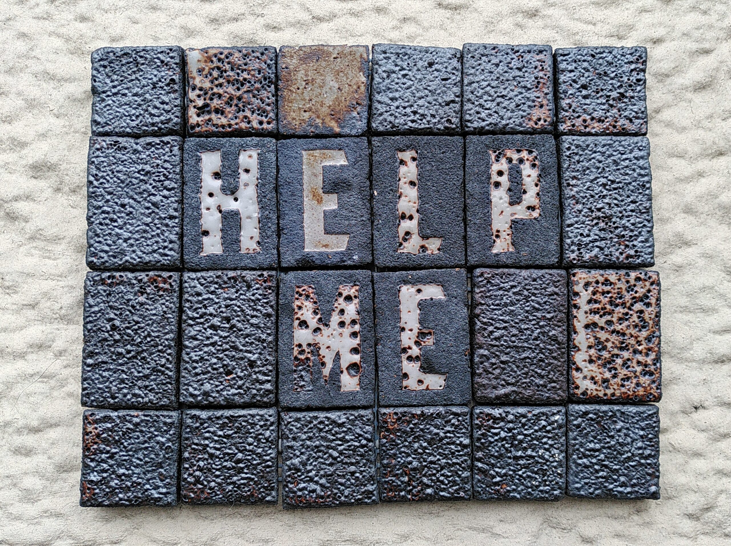 Mosaic tile "HELP ME" Ceramic mosaic tile. Rectangle. Black clay with a bubbly textured tiles. some glaze white/brown. Written HELP ME in capital letters.