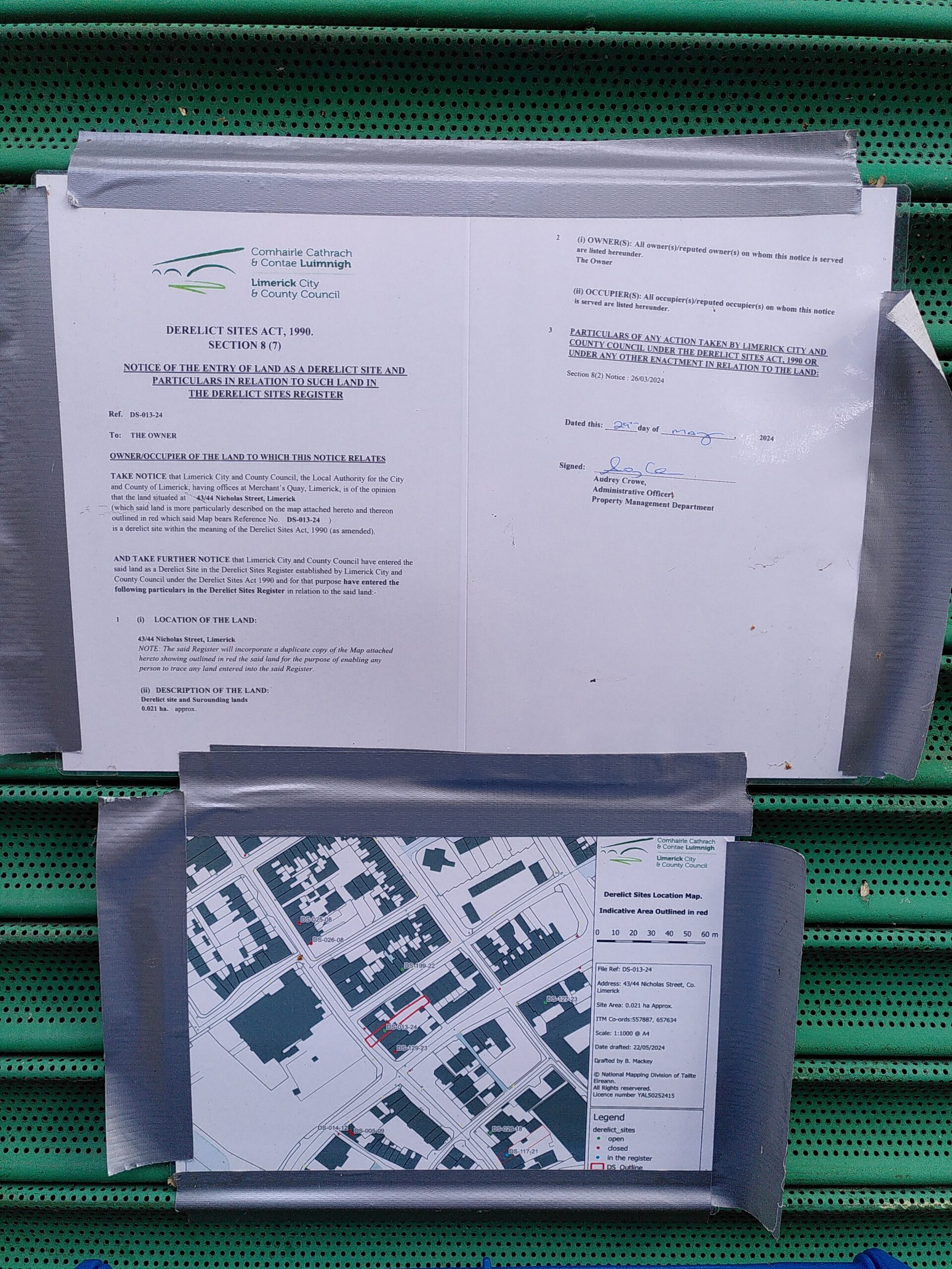 Dereliction notice A dereliction notice printed on paper and laminated with a map is taped with grey tape on a commercial like green metal shutter.
